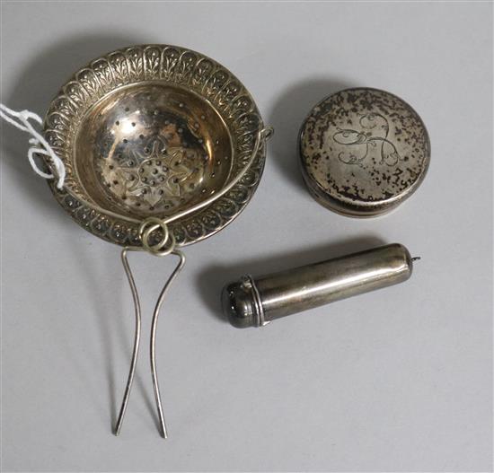 A George V silver tea strainer, a gold mounted cigarette holder with silver case and a silver bottle lid (3)
